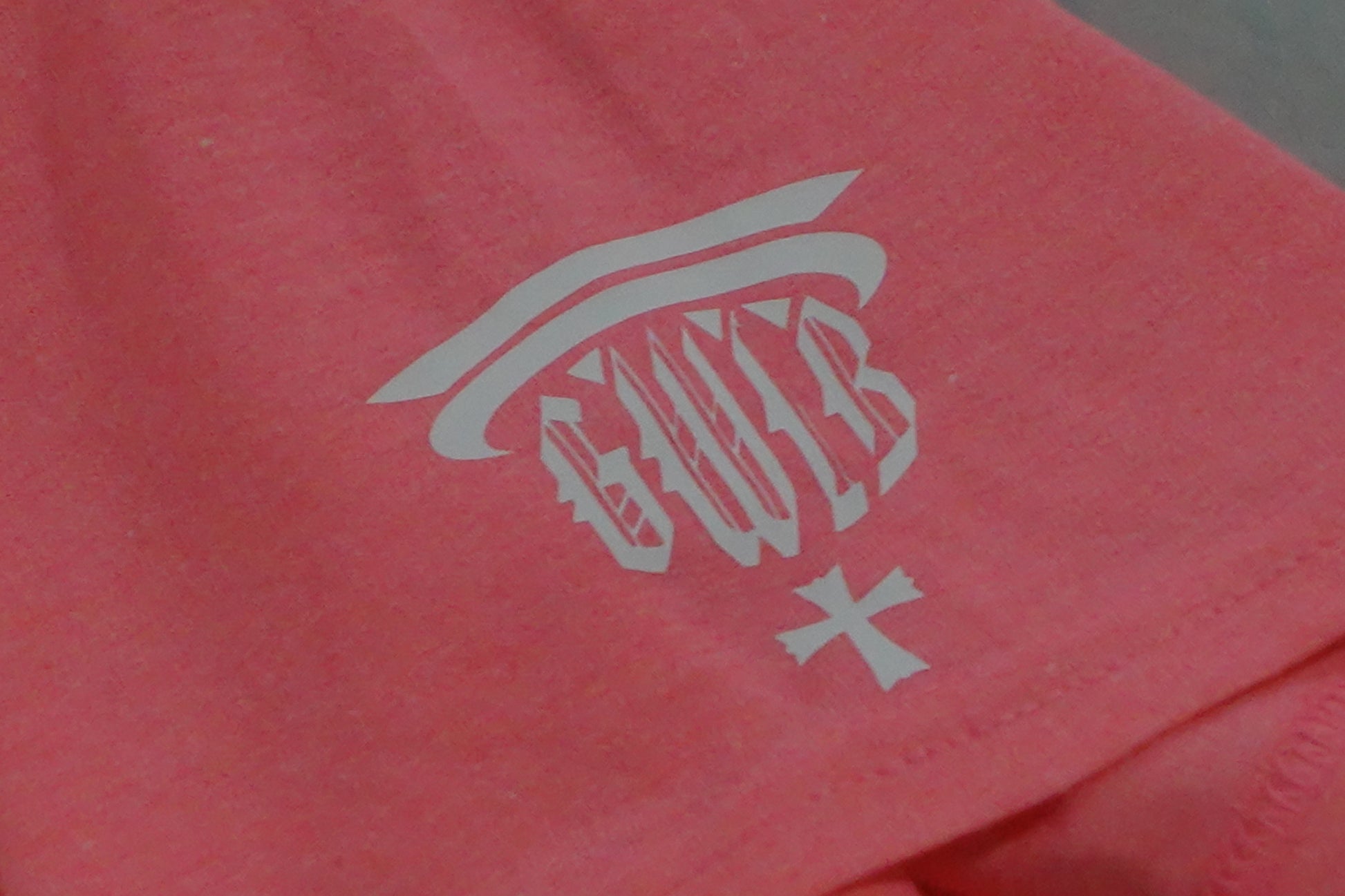 Close-up of a pink t-shirt with a white logo GWIB on the sleeve.