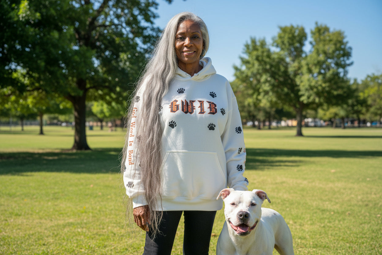Woman wearing a white GWIB-God Word Is Bond, hoodie with paw prints standing next to a white dog in a park.